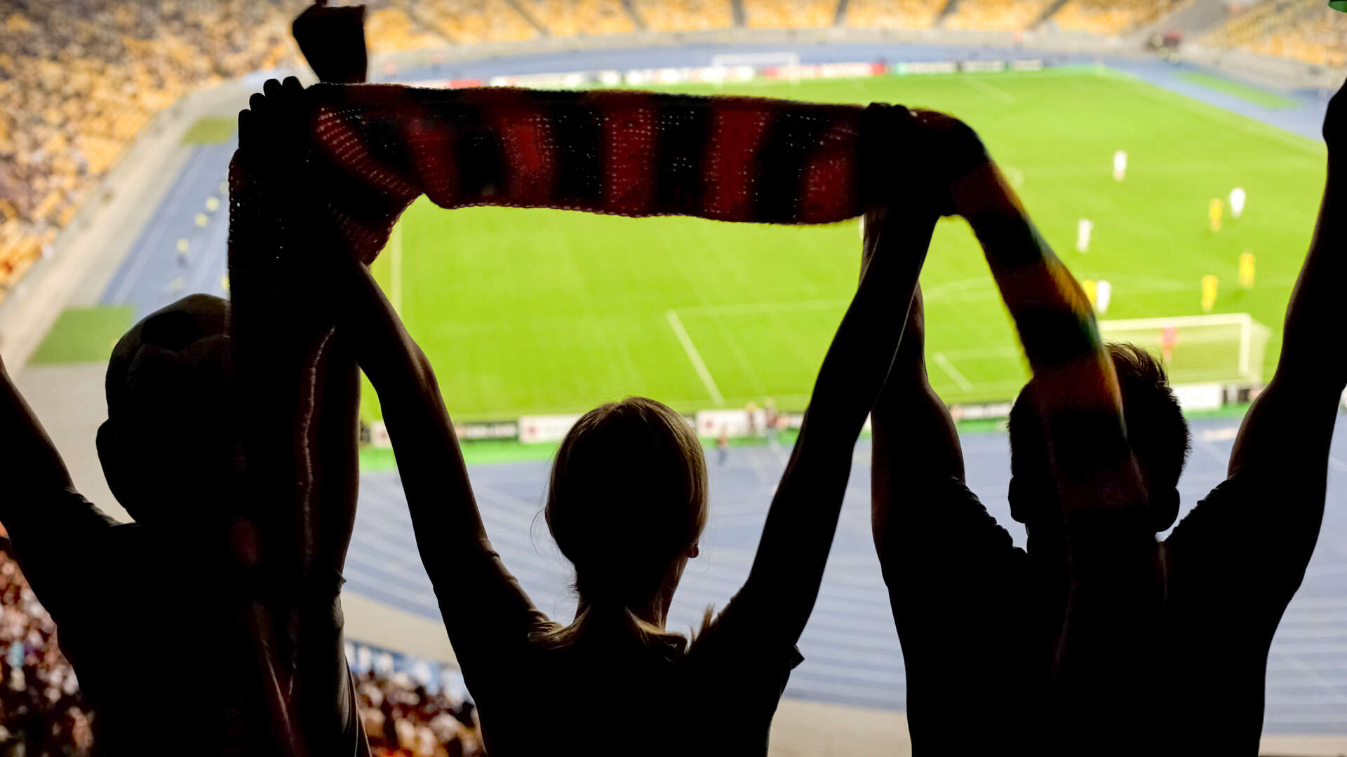 Supportere på en fotballtribune med kamp i bakgrunnen