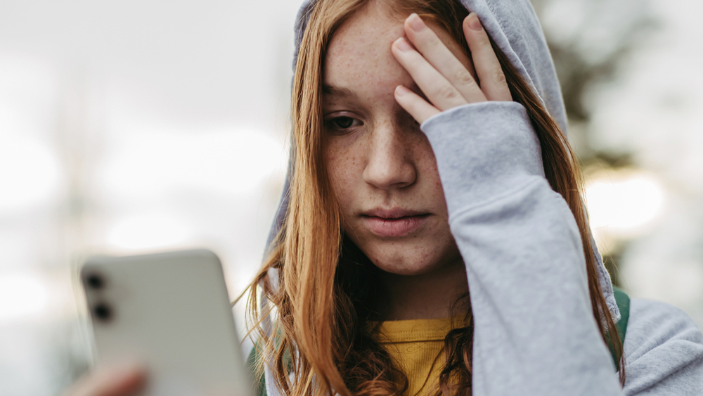 Jente med hettegenser ser bekymret på mobilen sin