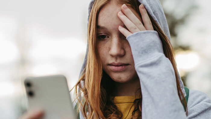 Jente med hettegenser ser bekymret på mobilen sin