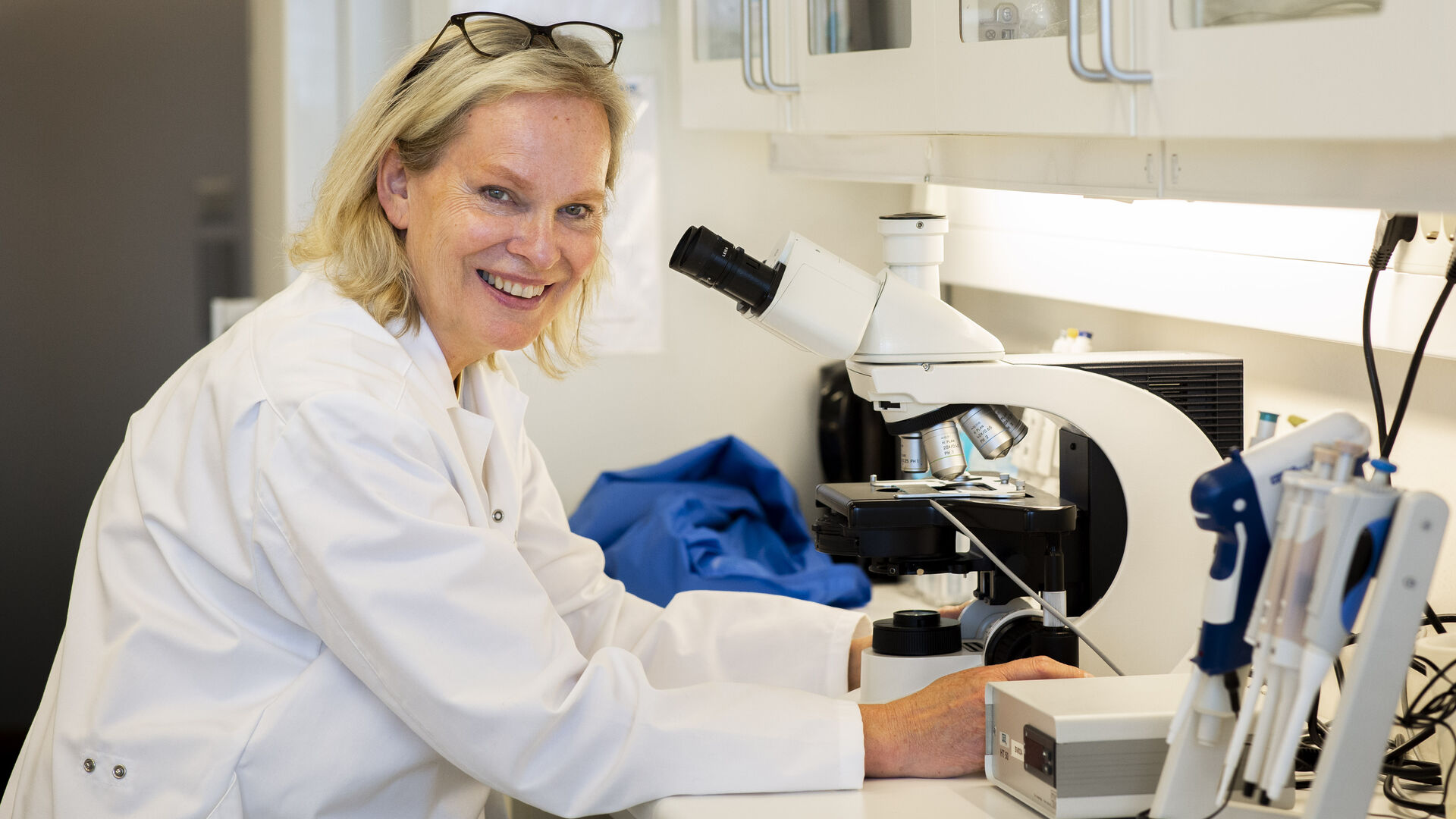 Bilde av Elisabeth Kommisrud foran et mikroskop med hvit frakk