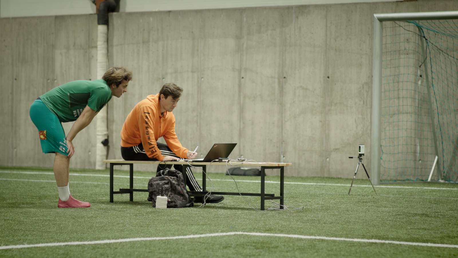 To stykker står over en PC og sjekker testresultater i en fotballhall
