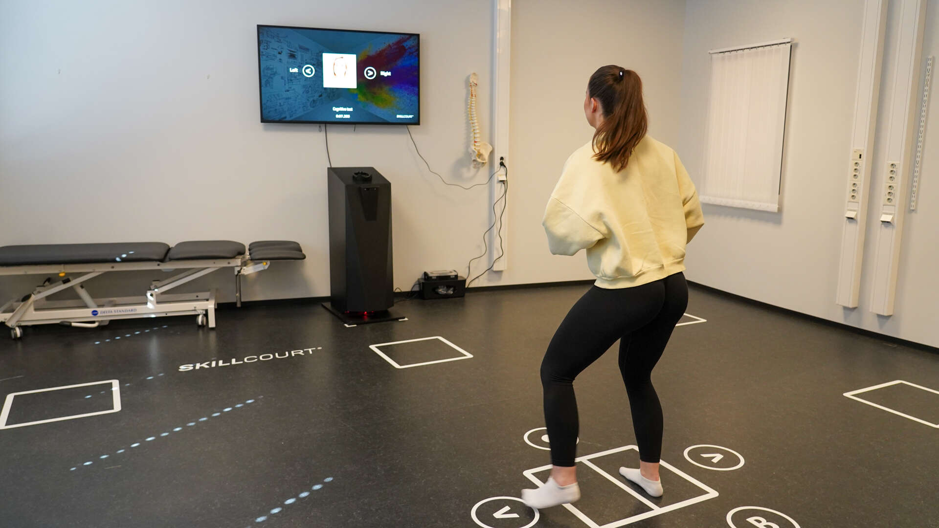 dame med gul genser og svart tights i et rom og gjør oppgaver