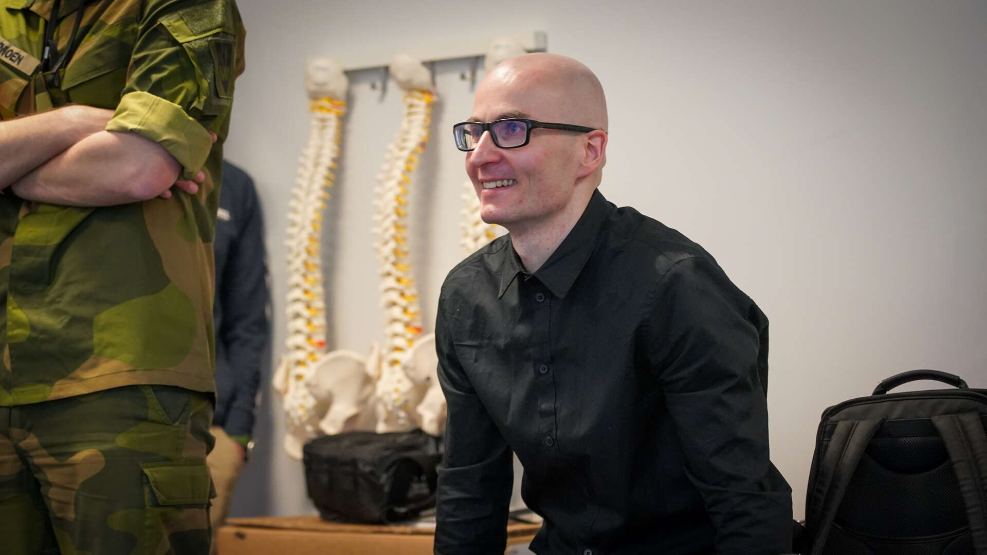 Mann med svart skjorte og briller ser ut i et rom