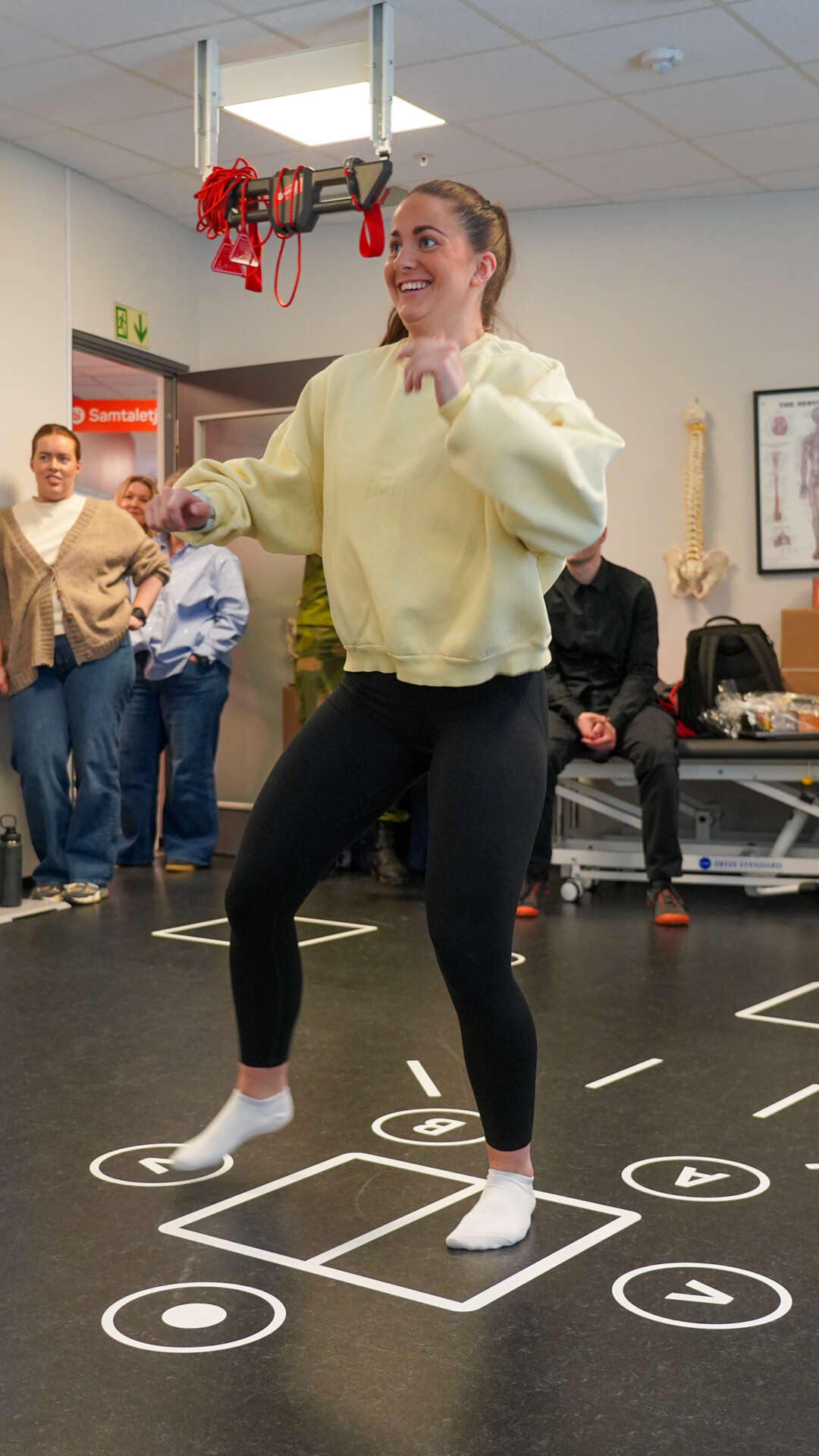 Dame med gul genser og svart tights gjør fysiske oppgaver i et rom