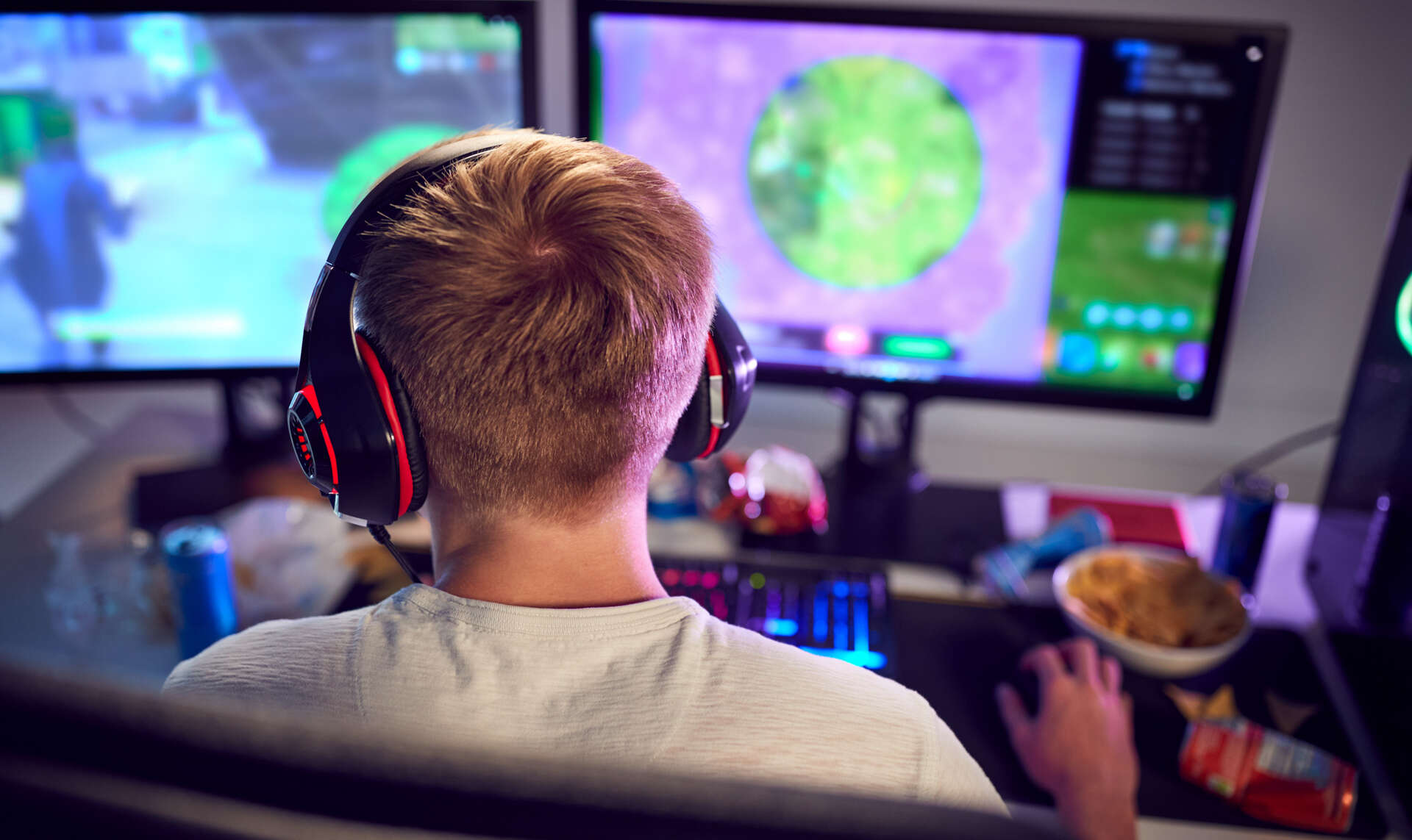 Gutt med ryggen til og med headset gamer på to skjermer