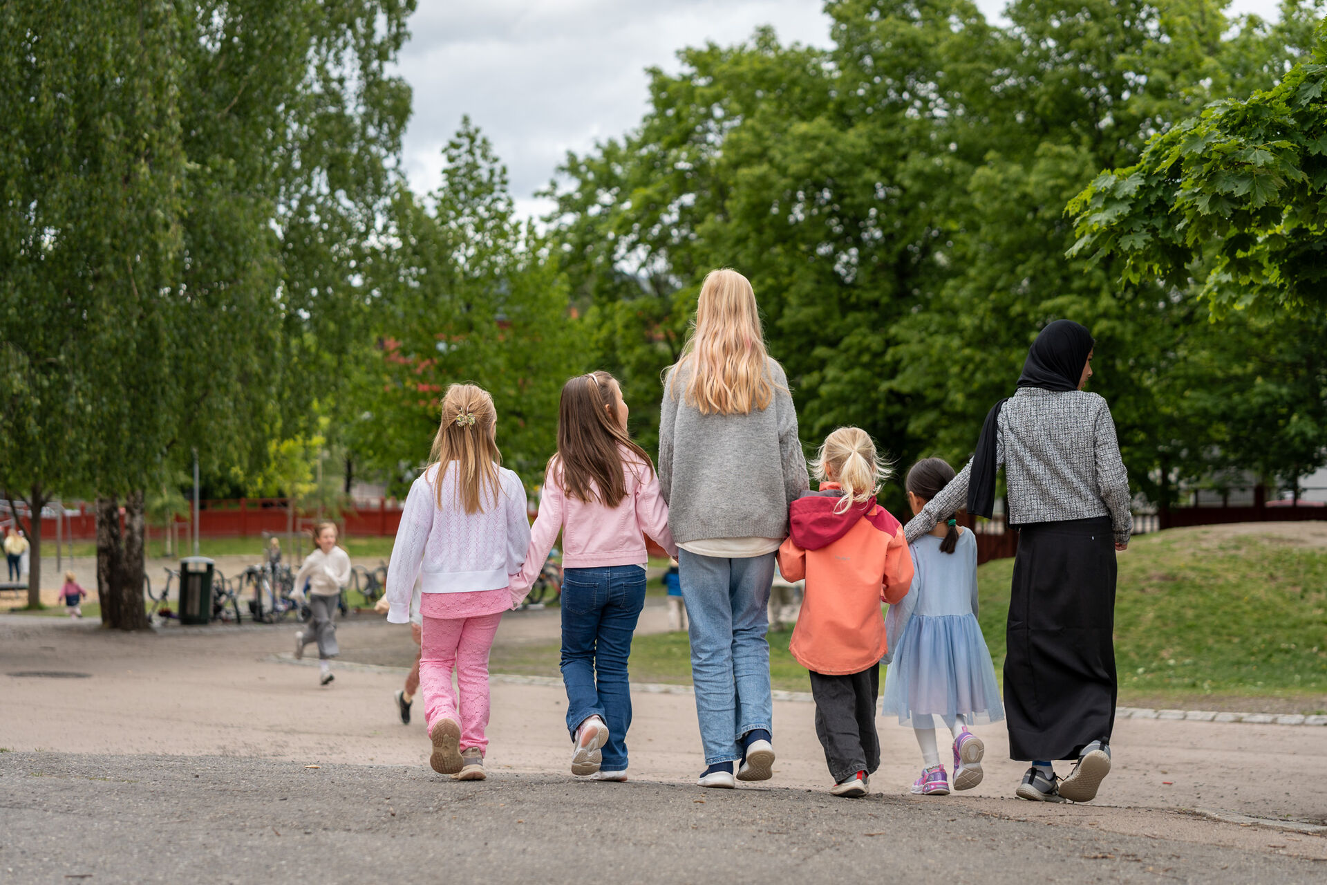 To faddere leier på flere skolestartere. Alle med ryggen til.