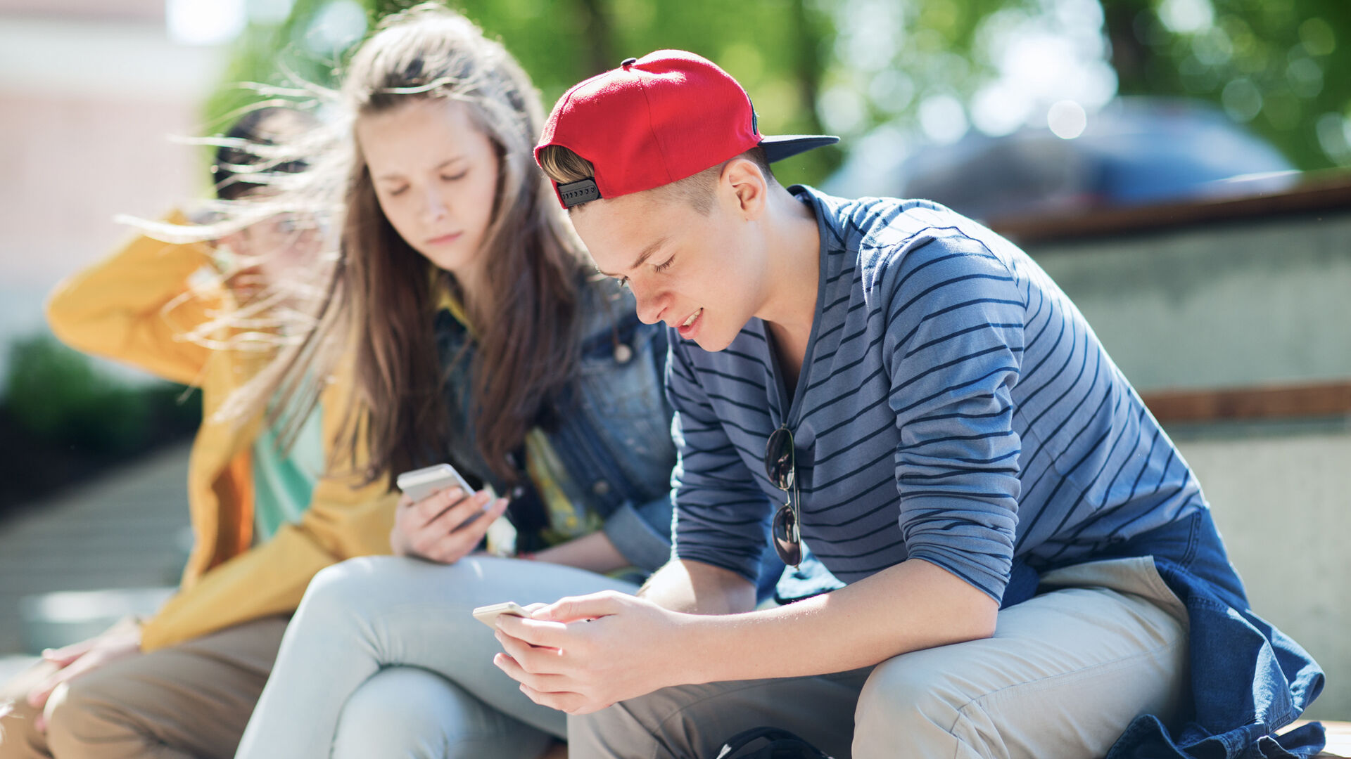 To ungdommer sitter ute og bruker mobilen sin