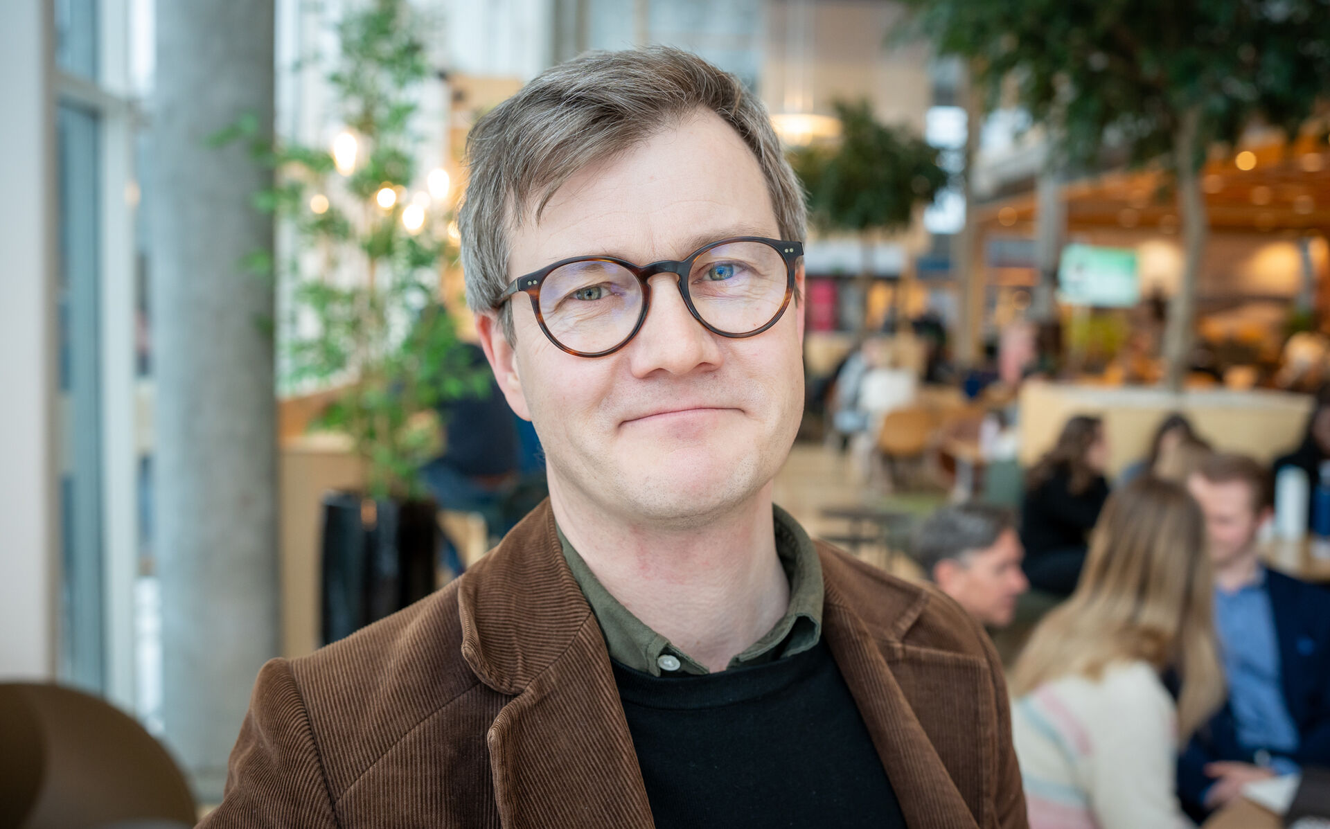 Mann med brun cordfløyelsjakke og briller i en kantine
