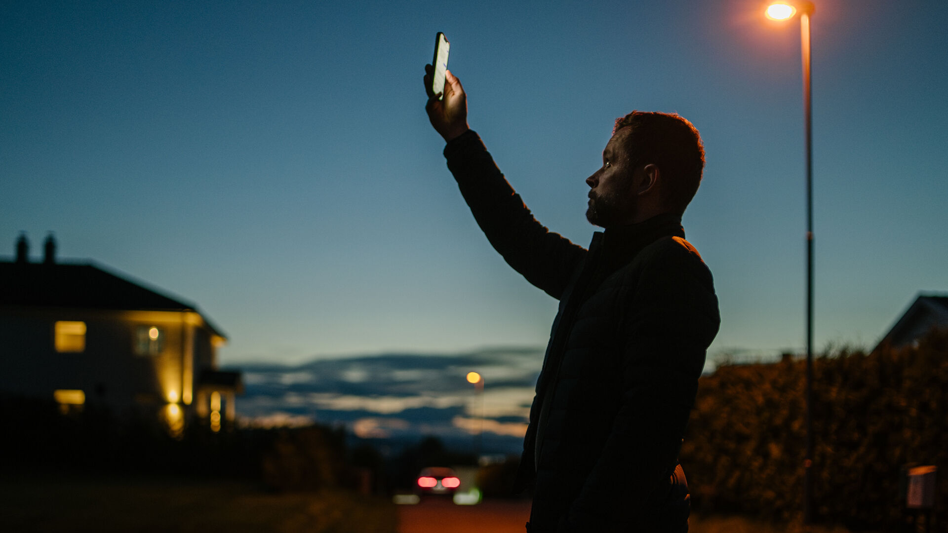 Mann står i mørket og holder mobilen sin opp mot himmelen