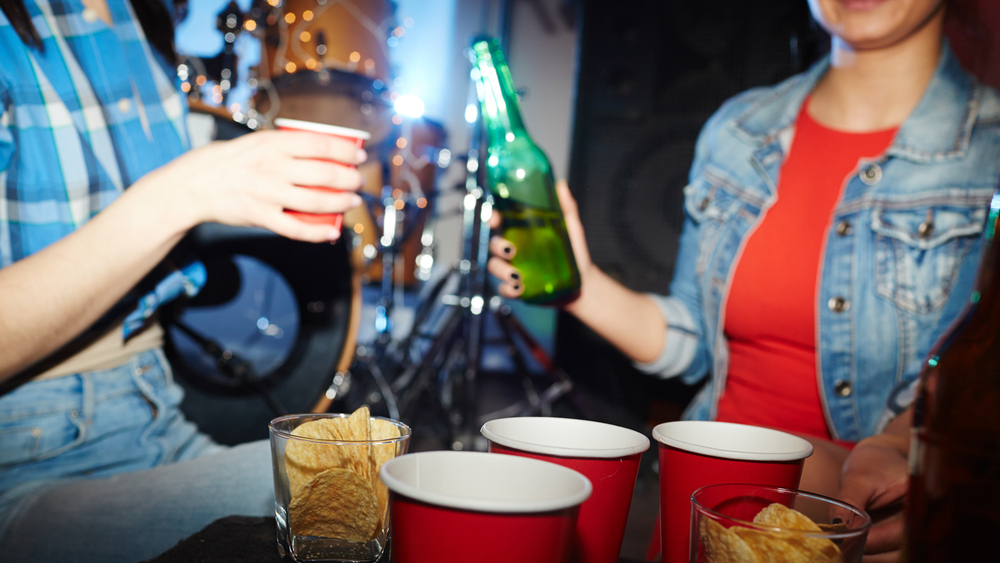 Ungdommer som sitter i en seng og noen stoler på et rom og drikker alkohol