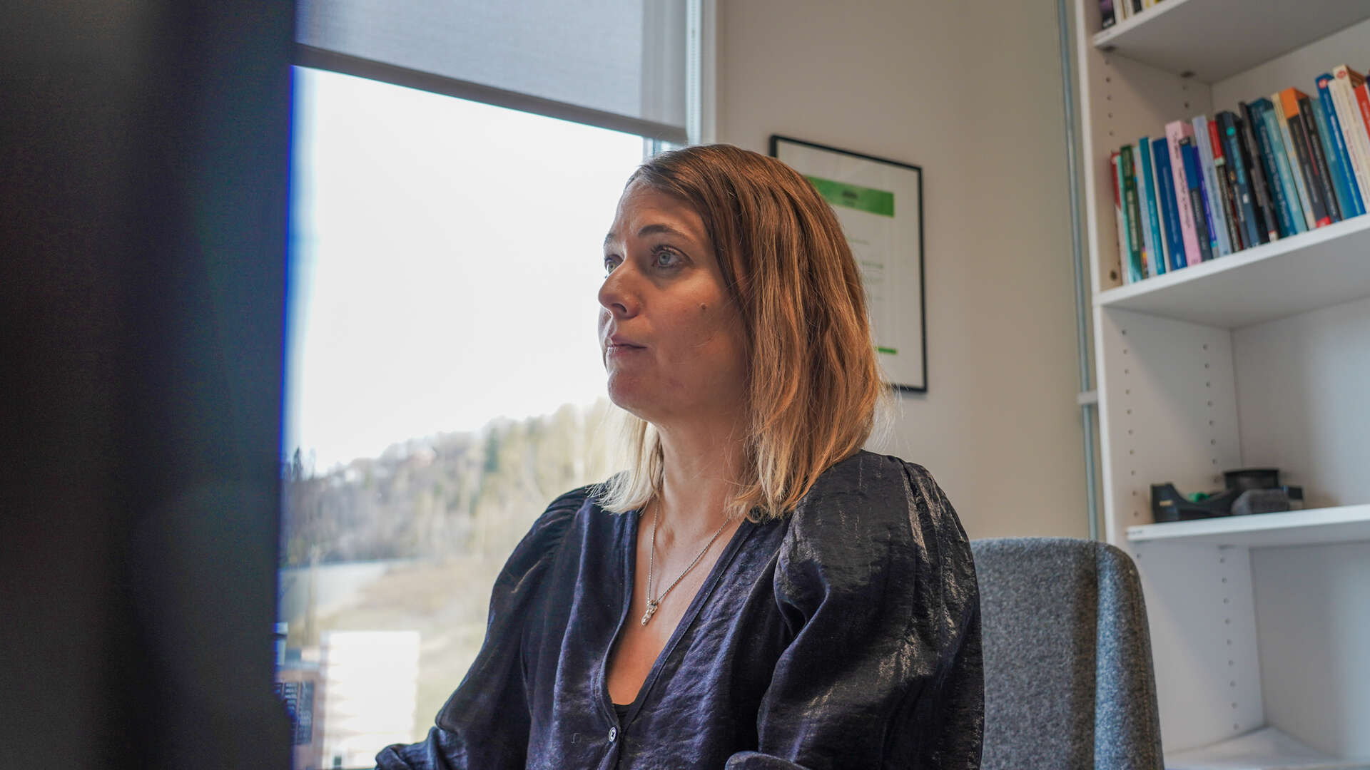 Dame ser på PC-skjermen inne på kontoret sitt ved pulten