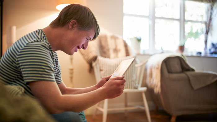 Bilde av ung mann med Downs syndrom som ser på nettbrett i en sofa
