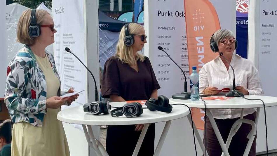 Tre damer med solbriller, headset og mikrofon. Den ene prater, de andre lytter. Alle har solbriller.
