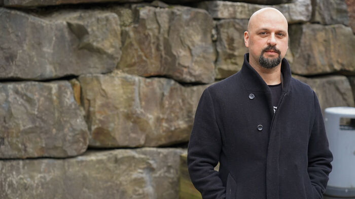 Khoury ser i kamera, står foran en steinmur