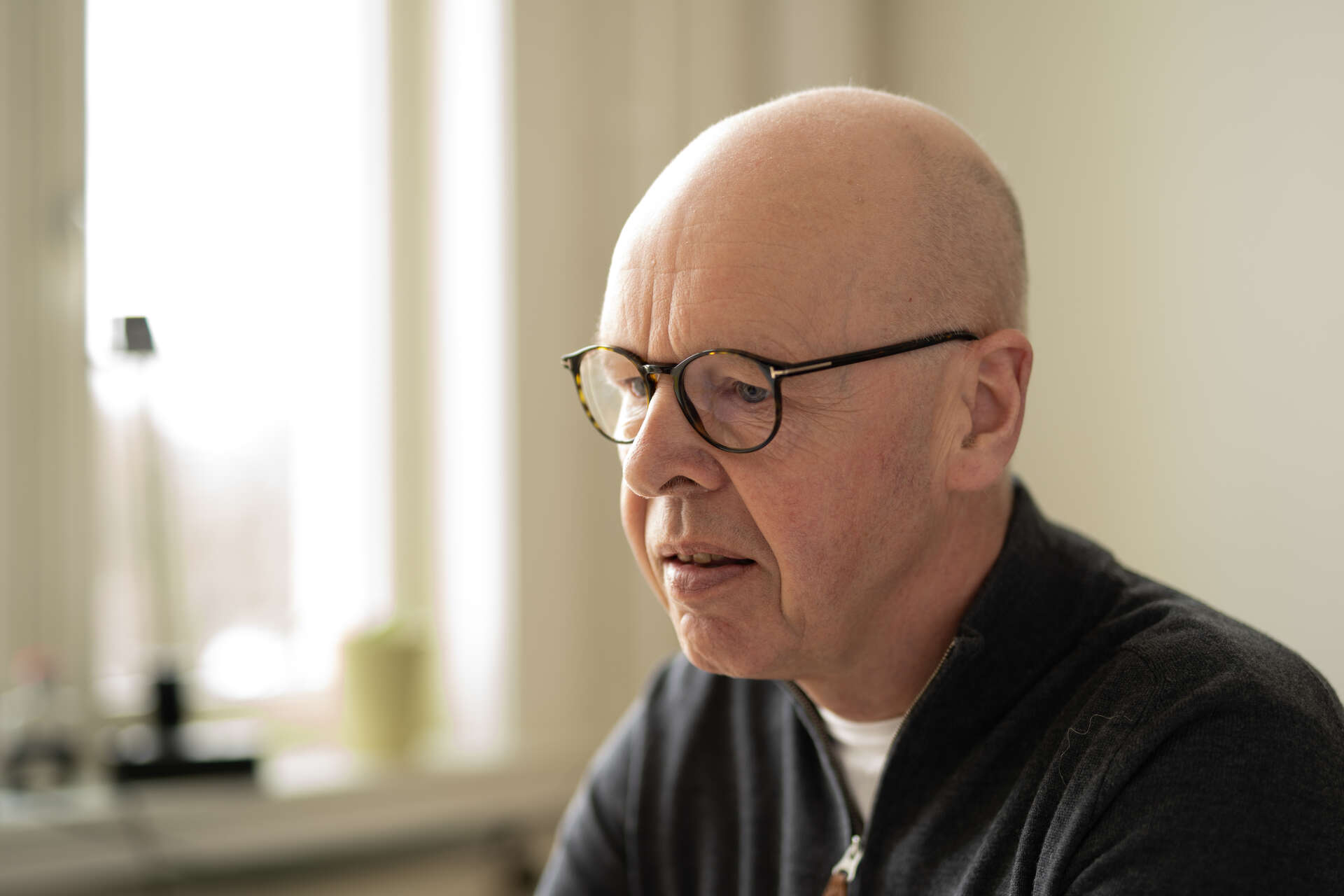 Mann uten hår og med briller sitter ved pult og ser på på PC