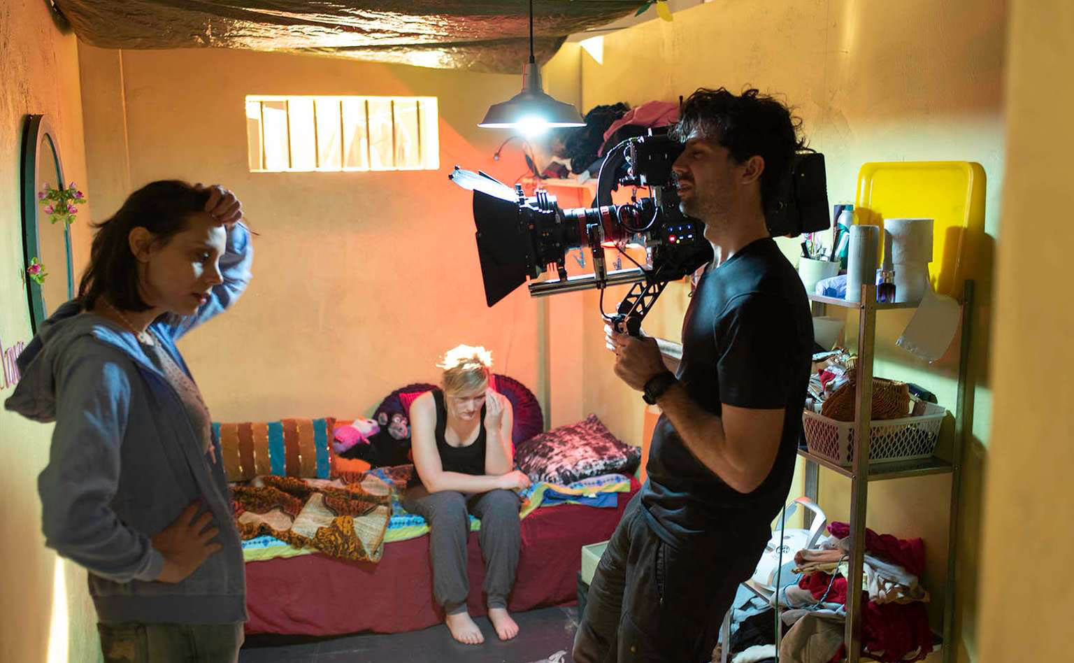 Innspilling av filmscene i lite kjellerrom; kvinne foran kamera holdt av mann.