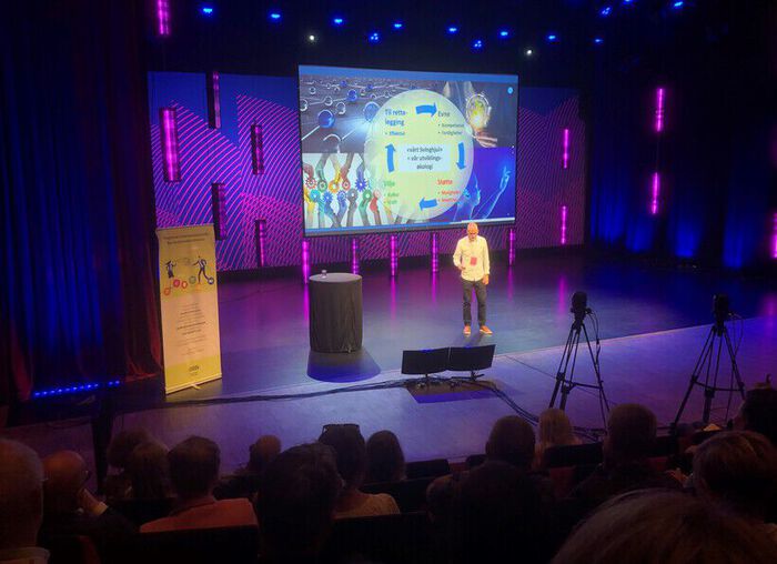 Man med power point på stor scene med masse lila og blått
