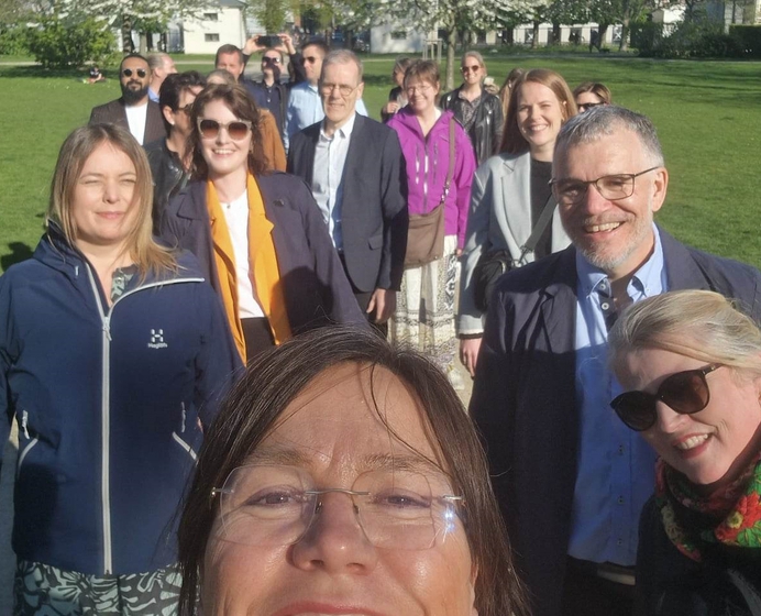 selfie av en dame med en gruppe mennesker og blomstrende trær bak seg
