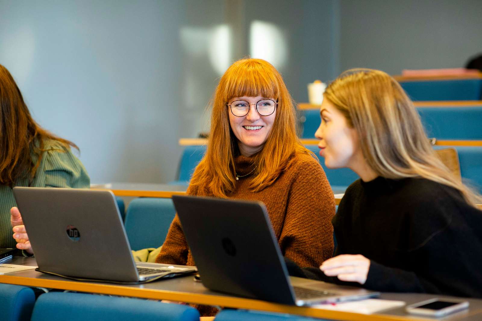 To voksne kvinnelige studenter i samtale bak pc'er.