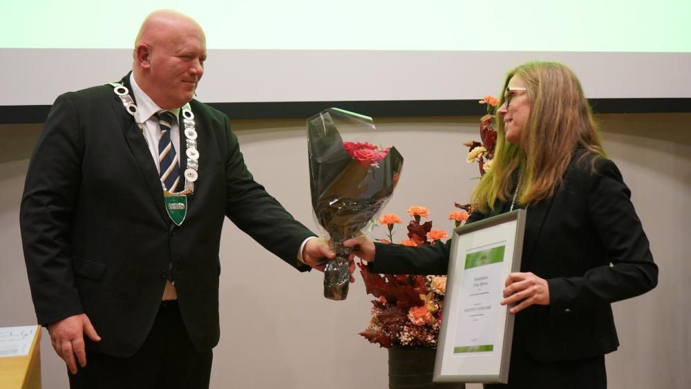 Rektor Peer Jacob Svenkerud deler ut blomster til Trine Bjerva som holder en diplom i hendene