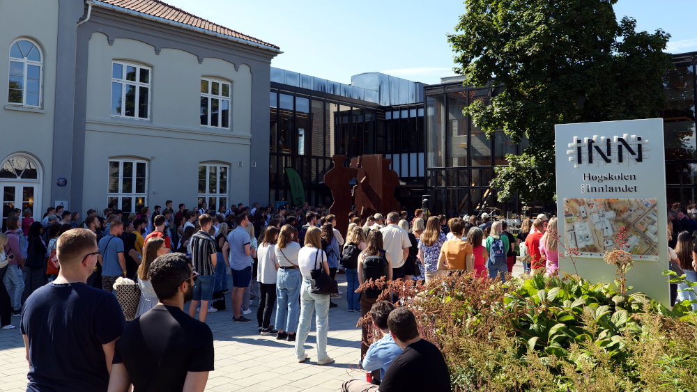 Mange studenter samlet foran høgskolebygget på Hamar, et skilt med HINNs logo er synlig