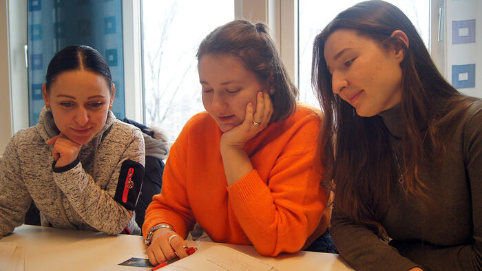 Three Ukranian students sitting together and reading a book. 