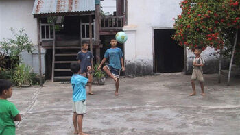 Bildet viser afrikanske barn som leker med fotball på en gårdsplass.