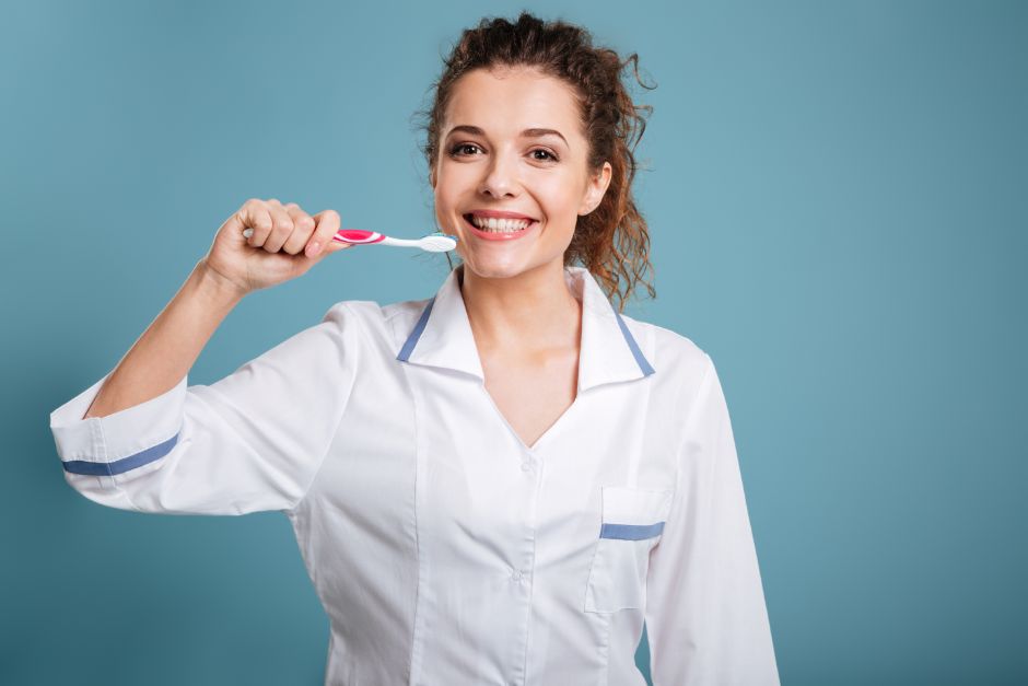 Smilende tannlegeassistent med en tannbørste i hånden