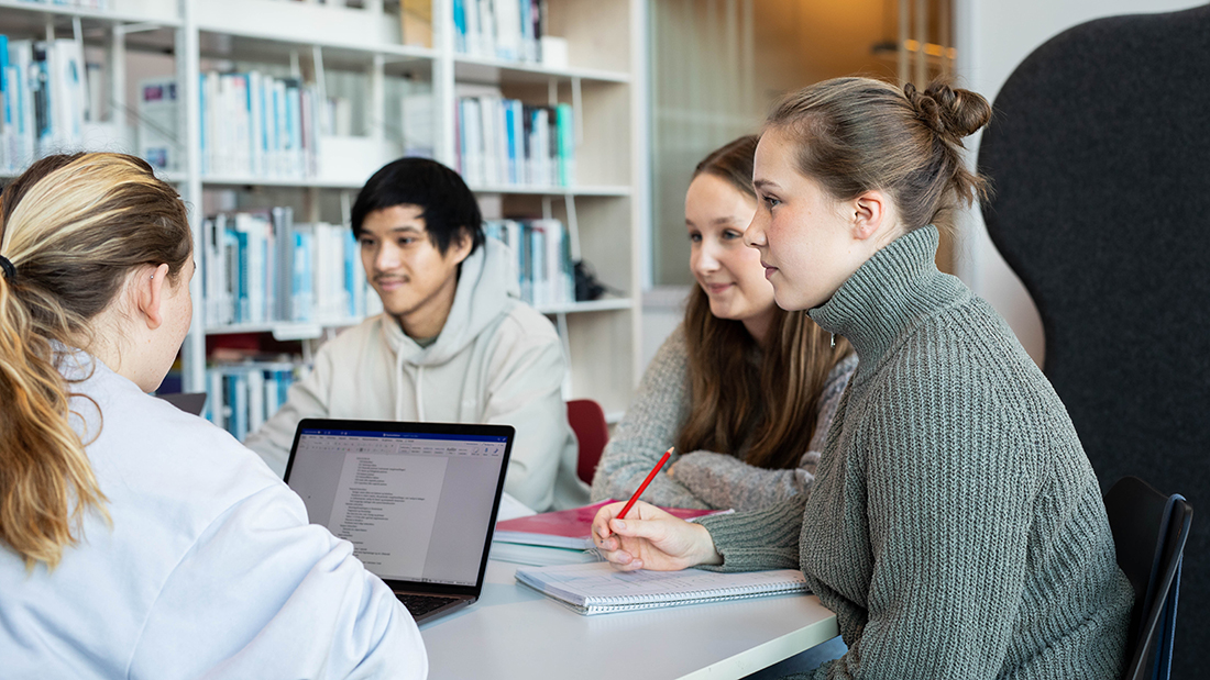 Fire studenter i lyse klær som jobber sitter ved et bord på biblioteket og jobber sammen. 