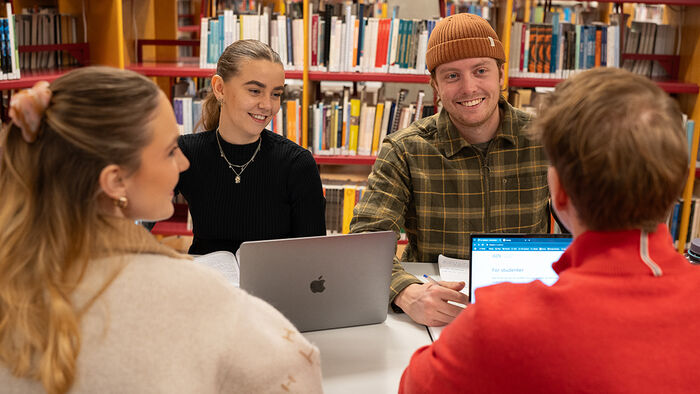 Fire smilende studenter på biblioteket. 