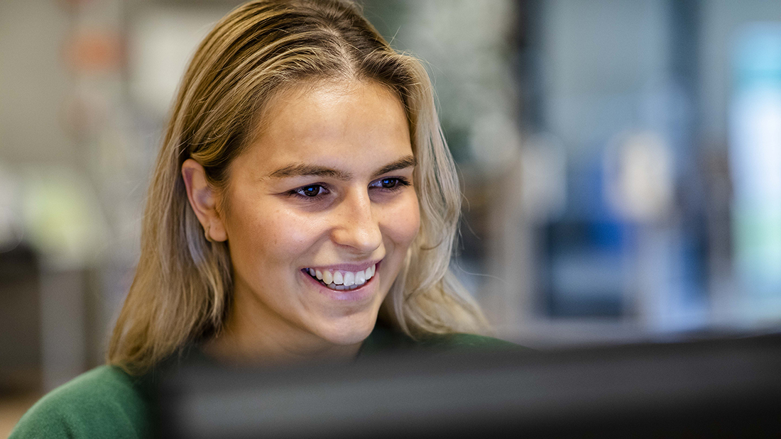 Smilende student som jobber på en PC. 