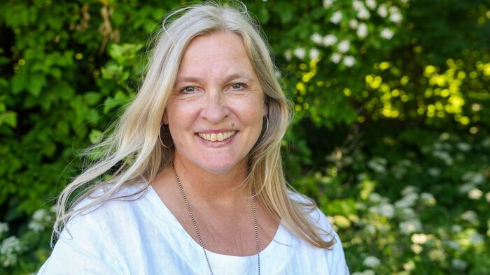 Portrett av Kjersti Normann med grønne vekster i bakgrunnen