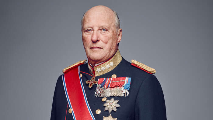 Portrettfoto av Kong Harald i mørk uniform, medaljer og rødt ordensbånd