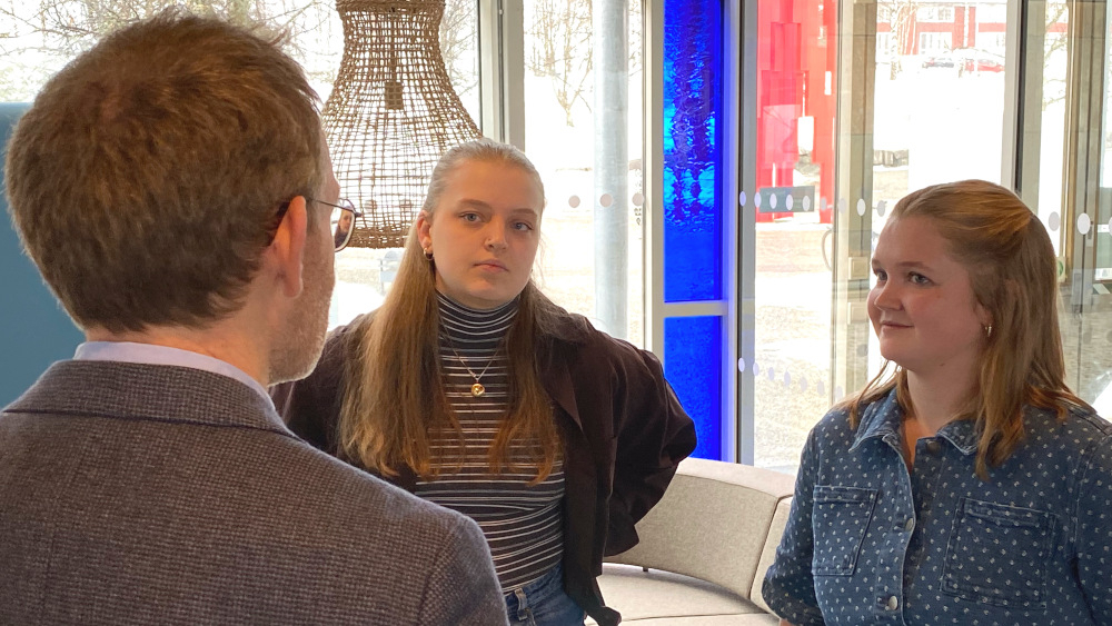 Ingeborg Kokkvoll og Tina Martinussen står med ansiktet mot kamera i samtale med Oddmund Løkensgard Hoel som vises bakfra