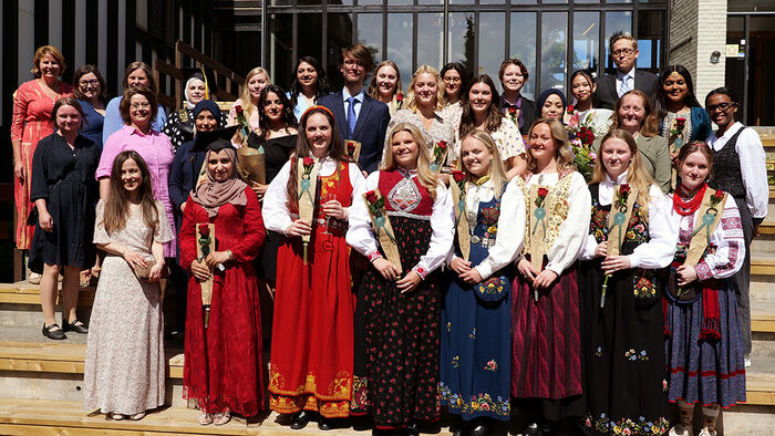 To studenter kledd i dress og bunad  som står ute i en grønn park. 