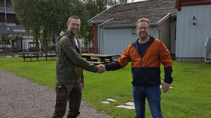 Two men shaking hands in front of Evenstad campus. 