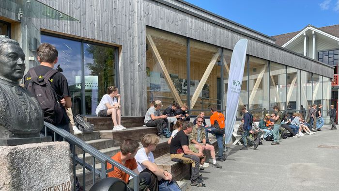Ungdommer sitter utenfor hovedbygg på studiested Evenstad i solen.