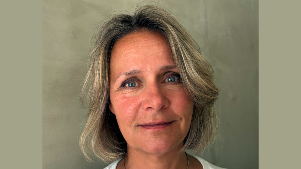Portrett av en smilende Karianne Eide-Longva med grå-grønn bakgrunn