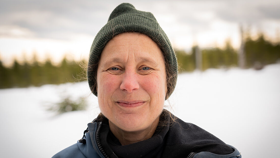 Portrait photo of a woman standing in a snowy landscape wearing a green woolen hat.