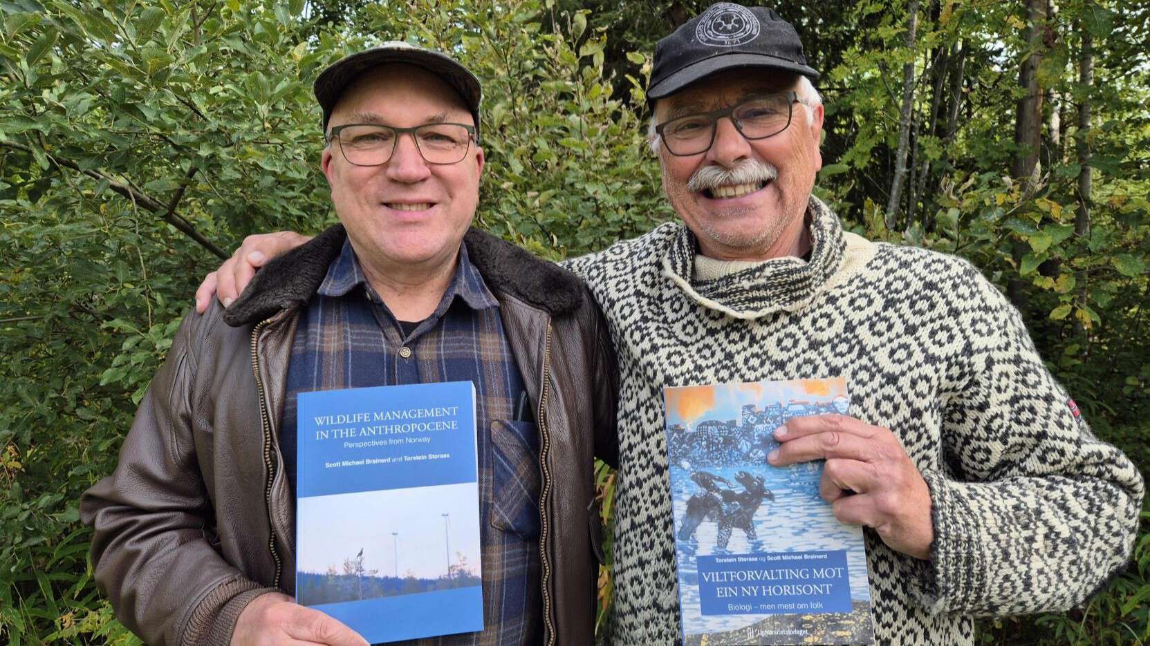 To menn holder hver sin bok opp og viser frem fremsiden av boka de selv har skrevet. Den til venstre er engelskspråkelig, mens den til høyre er på nynorsk.