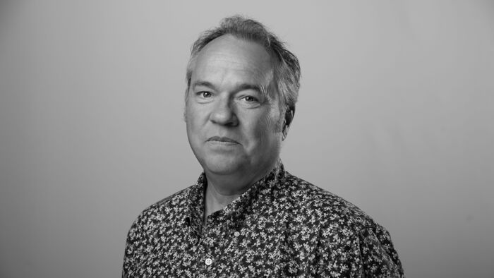 Svart hvitt protrett av Fredrik Graver i blomstrete skjorte på grå bakgrunn
