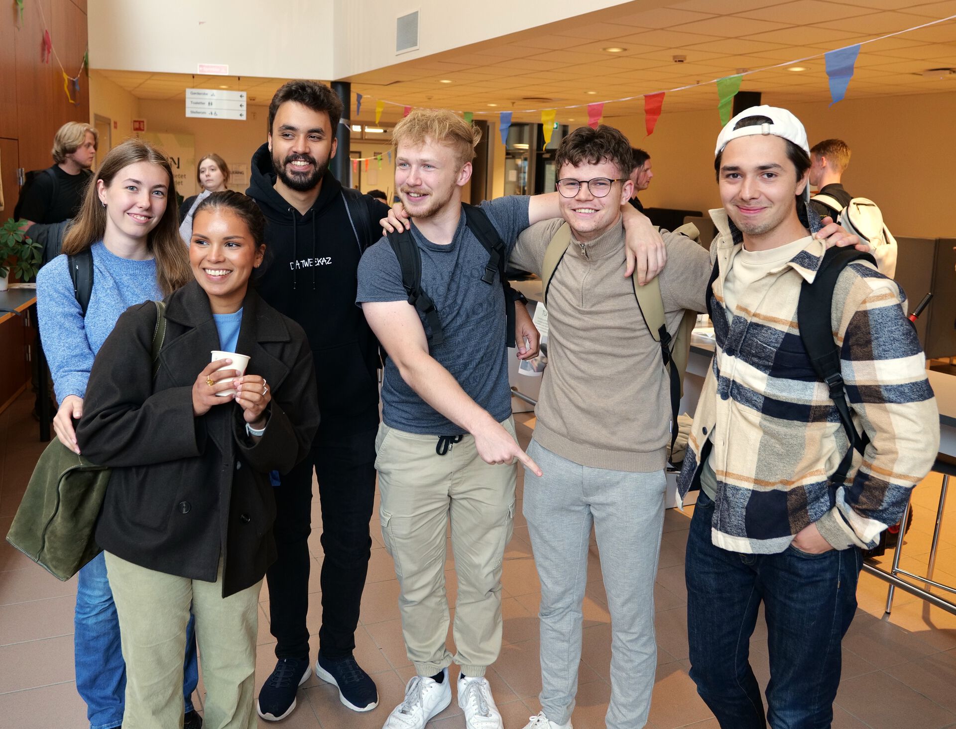 En gjeng studenter står og smiler på campus