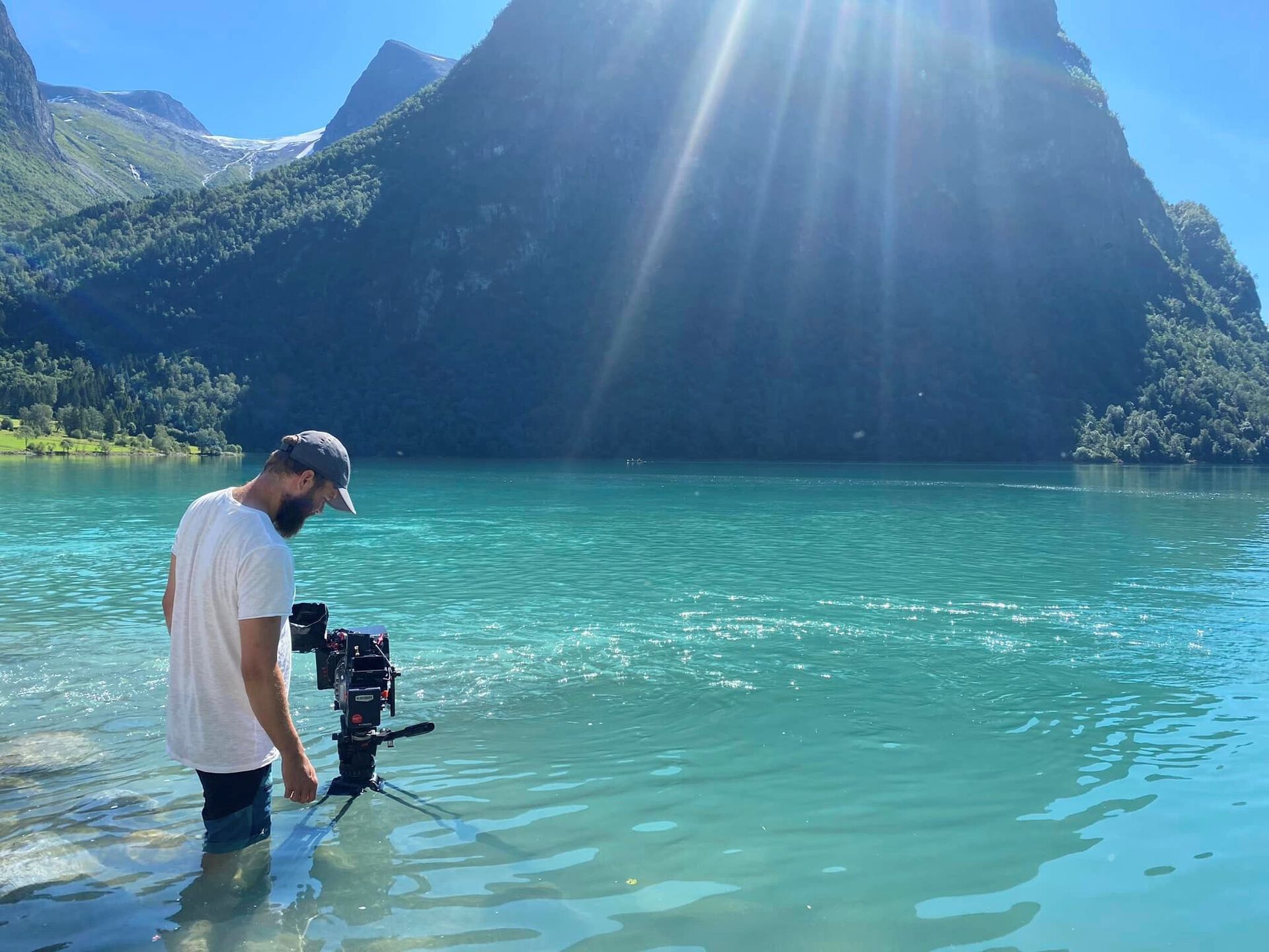 Lars som står ute i en innsjø med fjellrundt mens han fotograferer