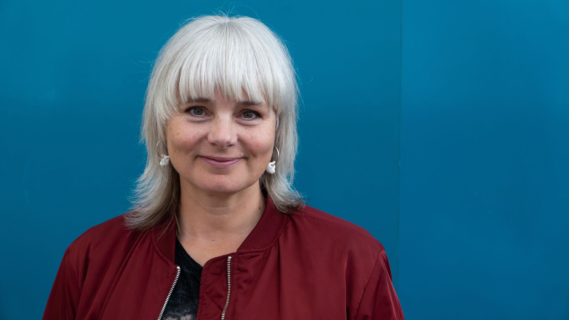 Portrett av førsteamanuensis Camilla Vanebo i rød jakke med turkis bakgrunn