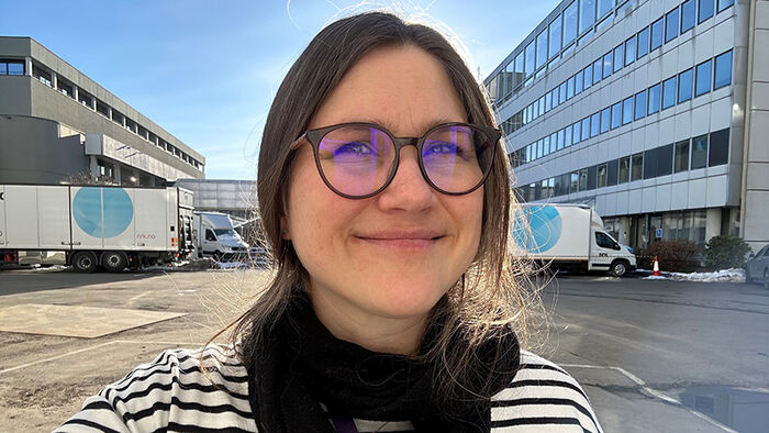 Portrett av Ingrid Løvsland i bakgården på NRK. Man skimter to lastebiler med NRK-logo i bakgrunnen. Ingrid har på seg stripete genser. 
