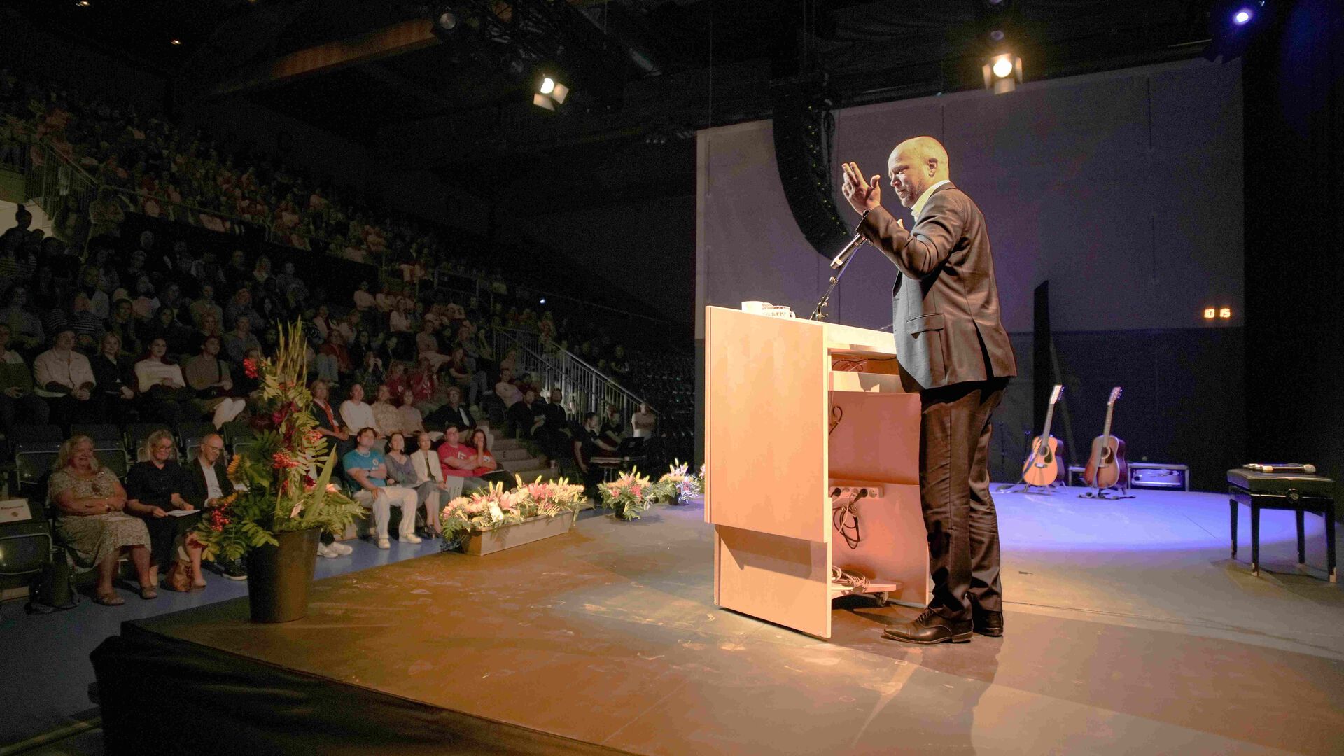Trygve Slagsvold Vedum står i lyset bak en talerstol, publikum sitter på trtibuner i mørket.