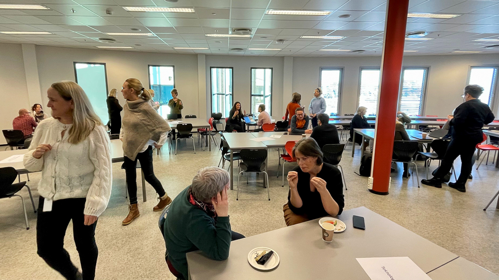 Mange folk som sitter og står rundt i et klasserom