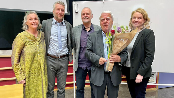 Bilde av fem personer i et auditorium som står på rekke. Den ene holder blomster i hendene