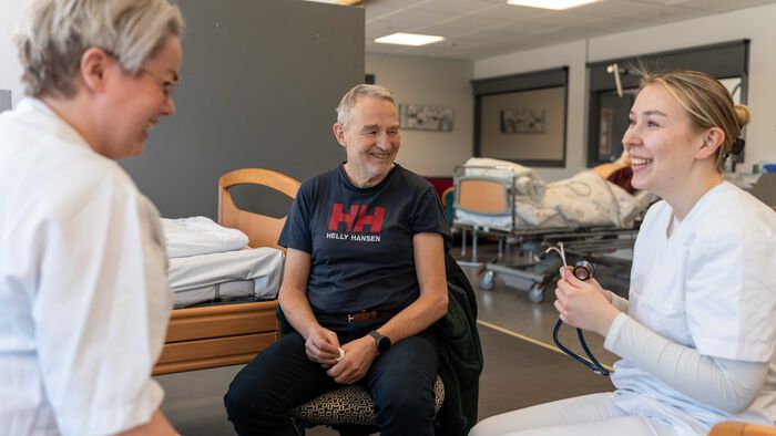 To sykepleierstudenter i hyggelig prat med en mannlig pensjonist.