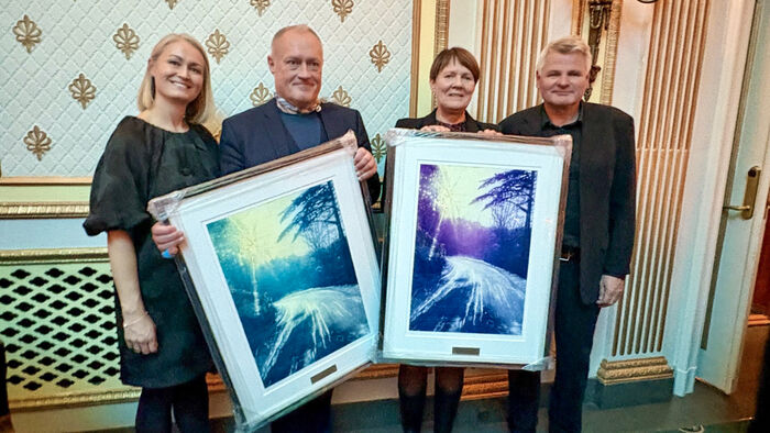 Fire personer står ved siden av hverandre med to store bilder i ramme foran seg